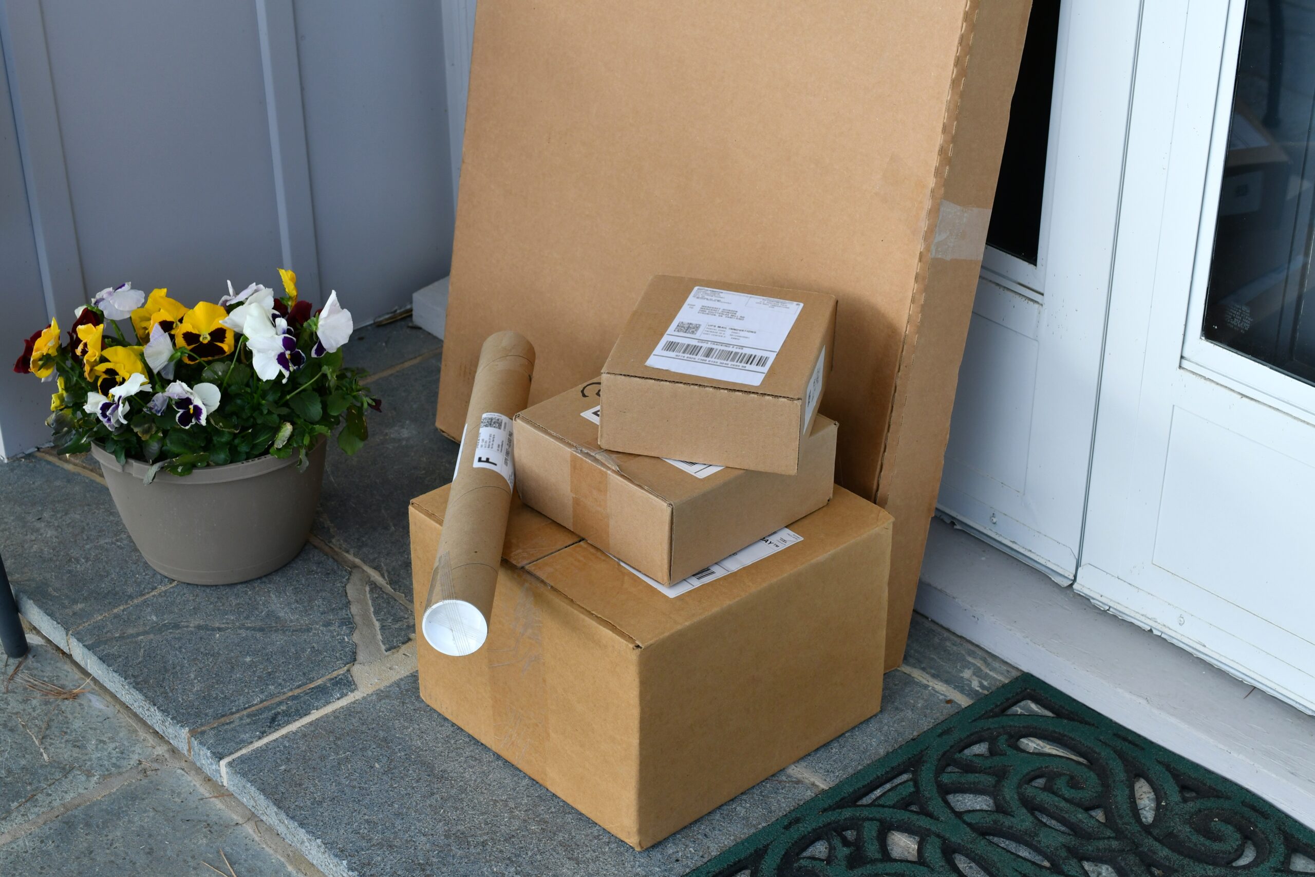 boxes-packages-mail-parcels-from-online-orders-on-2025-03-11-18-20-01-utc A stack of delivered ecommerce packages on a residential doorstep.